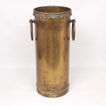 Bengaleiro de formato cilíndrico em metal dourado, com duas alças móveis laterais em argolas articuladas. Borda superior ornamentada por friso em relevo com motivos de folhas estilizadas de inspiração neoclássica. Apresenta pátina, oxidação e desgaste compatíveis com a idade e uso. Medidas: Alt.: 50 x Diam.: 21 cm.
