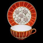 Xícara para chá em porcelana japonesa, bojo hemisférico assente sobre base circular, decoração policromada e em relevo composta por reservas florais estilizadas sobre fundo perolizado, faixa ornamentada por filetes verticais em laranja, azul, verde, branco e dourado, alças lateral curvada. Marca ao fundo JH acompanhada de caracteres japoneses. Medidas: Alt.: 4 x Comp.: 10 x Larg.: 8,5 cm. Alt.: 6 x Diam.: 13 cm.