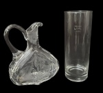 Conjunto em vidro e cristal, composto por licoreira/jarra lapidada, com alça e bico vertedor, decoração vegetal em lapidação profunda e base estrelada, acompanhada de copo graduado em vidro, marcado 0,4 L  Lausitz. Peças de caráter utilitário e decorativo. Apresentam sinais compatíveis com uso e idade. Medida do maior 18cm.