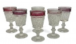 Conjunto com 6 taças antigas em cristal prensado, corpo lapidado com padrão geométrico e borda superior com faixa em tom rubi. Hastes e bases trabalhadas, conferindo elegância e charme clássico à mesa. Contém desgastes do tempo. Mede 11cm de altura.