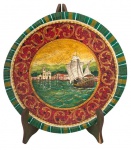 Medalhão decorativo em madeira policromada, com rica ornamentação em relevo e pintura manual. Cena central representando paisagem litorânea com embarcação à vela e arquitetura colonial, cercada por moldura em tons de vermelho, verde e dourado com elementos arabescados. Assinado. Peça de forte apelo decorativo, ideal para composição de parede. Mede 37cm de diâmetro.
