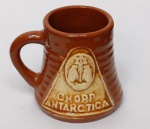 Mini Caneca Chopp Antarctica Vintage  Cerâmica Colecionável  Brinde RetrôAntarctica (Logotipo clássico com os pinguins no medalhão).Material: Cerâmica esmaltada (grês) em tom marrom caramelo.Estilo: "Mini Stein" promocional, com corpo canelado e logotipo em relevo na cor creme/areia.