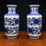 Elegante par de vasos em porcelana esmaltada, decorados em tradicional padrão azul sob fundo branco, apresentando rica ornamentação floral estilizada, arabescos e caracteres orientais na região do colo.As peças exibem desenho inspirado nos modelos clássicos da porcelana chinesa, com refinado repertório decorativo de influência Ming/Qing, destacando composição harmoniosa, esmaltação vítrea e acabamento de forte apelo ornamental.