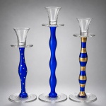 ANNE NILSSON  Conjunto de castiçais em vidro artístico azulElegante conjunto composto por três castiçais de design assinado por Anne Nilsson, executados em vidro artístico nas tonalidades azul cobalto e cristal incolor, caracterizados por linhas esculturais, hastes sinuosas e refinado minimalismo escandinavo.As peças apresentam distintas composições decorativas  lisa, pontilhada e listrada  valorizando a linguagem contemporânea e o apuro formal característicos da designer sueca. Os elementos em vidro translúcido, associados às bases circulares e aos receptáculos superiores em cristal, conferem equilíbrio, leveza visual e marcante sofisticação ao conjunto.Obras representativas do design nórdico contemporâneo, conciliando funcionalidade, elegância