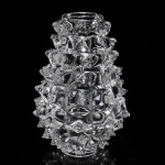 BAROVIER & TOSO  Vaso Rostrato, década de 1940Importante vaso Rostrato em vidro artístico de Murano, manufatura Barovier & Toso, datado da década de 1940, exemplar emblemático do design italiano do pós-guerra e da excelência vidreira veneziana.Executado em vidro transparente moldado, apresenta a célebre técnica Rostrato, caracterizada pela superfície integralmente ornamentada por projeções pontiagudas (rostri), criando extraordinário efeito escultórico, luminoso e tátil.Modelo de forte presença arquitetônica e linguagem modernista, traduz o virtuosismo técnico e a inovação formal associados à histórica casa Barovier & Toso, referência incontornável da produção muranesa do século XX.Peça de elevado interesse colecionístico, representativa do auge criativo do design italiano em vidro artístico.