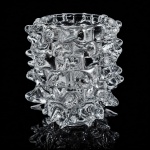 BAROVIER & TOSO  Vaso Rostrato, década de 1940Importante vaso Rostrato em vidro artístico de Murano, manufatura Barovier & Toso, datado da década de 1940, exemplar emblemático do design italiano do pós-guerra e da excelência vidreira veneziana.Executado em vidro transparente moldado, apresenta a célebre técnica Rostrato, caracterizada pela superfície integralmente ornamentada por projeções pontiagudas (rostri), criando extraordinário efeito escultórico, luminoso e tátil.Modelo de forte presença arquitetônica e linguagem modernista, traduz o virtuosismo técnico e a inovação formal associados à histórica casa Barovier & Toso, referência incontornável da produção muranesa do século XX.Peça de elevado interesse colecionístico, representativa do auge criativo do design italiano em vidro artístico