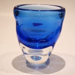 Vaso artístico em Murano, em intensa tonalidade azul cobalto, apresentando espessa parede de vidro soprado e elegante base facetada translúcida.Peça de desenho minimalista e forte presença escultórica, destacando a tradicional excelência veneziana no trabalho do vidro artístico. A coloração por óxidos  com característica fluorescência associada ao uso de urânio em determinadas formulações