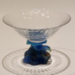 Centro de mesa francês DAUM, em cristal artístico de excepcional qualidade, apresentando elegante copa translúcida apoiada sobre base escultórica em pâte de verre, em delicado degradê âmbar.A composição revela o refinamento característico da célebre manufatura francesa, com modelagem orgânica inspirada na natureza, rica textura e notável efeito luminoso proporcionado pelo trabalho artesanal do cristal.