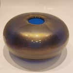 Vaso Sommersi Oro  Venini, Itália, 1993.Elegante exemplar do célebre design italiano em vidro artístico, executado pela renomada manufatura Venini, Murano. A peça apresenta composição em técnica sommerso, caracterizada pela sobreposição de camadas vítreas translúcidas, enriquecidas por delicadas inclusões douradas (oro), criando notável profundidade óptica e sofisticado efeito luminoso.De forma orgânica e escultural, o vaso evidencia refinado equilíbrio entre transparência, densidade cromática e o brilho sutil das partículas metálicas, atributos emblemáticos da tradição vidreira veneziana do final do século XX.