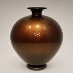 Vaso Sommersi Oro  Venini, Murano, Itália.Importante exemplar do vidro artístico italiano produzido pela tradicional manufatura Venini, reconhecida internacionalmente por sua excelência técnica e linguagem estética refinada.A peça apresenta elegante corpo globular de forte presença escultórica, com delicado colo curto e composição executada na célebre técnica Sommersi, marcada pela sobreposição de camadas vítreas translúcidas. O acabamento evidencia rica textura pontilhada com inclusões metálicas douradas (oro), criando sofisticado efeito luminoso, profundidade visual e notável densidade cromática.De desenho minimalista e monumental, o vaso traduz com precisão a linguagem do design muranês contemporâneo, unindo equilíbrio formal, virtuosismo artesanal e excepcional qualidade óptica.
