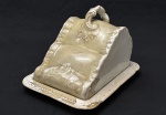 Staffordshire, Inglaterra. Antiga e rara queijeira/manteigueira em faiança inglesa,tampa em modelagem orgânica, com elegante pega em formato naturalista, além de acabamento em tonalidade creme. A base ostenta marca `Booths – Staffordshire`, reconhecida manufatura inglesa de destaque entre o final do século XIX e início do século XX. peça de caráter utilitário e decorativo que pertenceu ao histórico acervo da icônica Confeitaria Colombo, referência da belle époque carioca e patrimônio da gastronomia brasileira. Peça de grande apelo histórico e decorativo, ideal para compor ambientes clássicos, mesas postas, coleções de hotelaria antiga ou acervos ligados à memória da gastronomia e das antiguidades inglesas. Apresenta marcas naturais do tempo, craquelados, desgastes no esmalte e pequenas perdas e restauro. Medidas: 20 x 22 x 27 cm. 