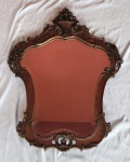 Espelho de parede com moldura em madeira ricamente entalhada, decorada com volutas, flores e cesto floral em relevo no coroamento, apresentando elegante desenho curvilíneo de influência rococó/francesa.. Medindo: 90 x 66 cm. ponta colocada, necessário restauro.