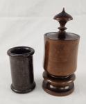 Conjunto de duas peças em madeira torneada, composto por recipiente com tampa e copo, em tonalidade escura com acabamento polido. Apresentam corpo cilíndrico com base levemente alargada e tampa com pega em formato cônico. Dimensões: maior 22 x 9 cm; menor 12 x 7 cm. 