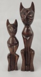 Par de esculturas em madeira entalhada, representando figuras estilizadas com traços alongados e expressão marcante, de inspiração étnica. Dimensões: 25,5 cm e 20 cm. 