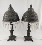 Imponente par de abajures confeccionados em bronze, com cúpulas ricamente trabalhadas em relevo e detalhes vazados, adornadas com aplicações decorativas em pedras coloridas. As bordas são finalizadas com franjas de pingentes em cristal lapidado. Bases em bronze com desenho ornamental, estilo oriental/otomano. Medidas aproximadas: 54 cm de altura x 23 cm de diâmetro. Poucos pingentes soltos. 