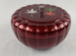 Caixa decorativa vintage com tampa em material sinteco de formato circular, com corpo em material sintético moldado em gomos e acabamento em tom vermelho escuro. Tampa decorada com delicado motivo de folhas estilizadas em policromia (verde, branco e laranja), com puxador central em metal. Medidas: 11 x 18 cm. 