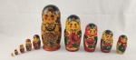 Boneca russa tipo matrioska em madeira, pintada à mão, composta por conjunto com 10 peças encaixáveis. Apresenta decoração policromada com figura feminina estilizada e motivos florais. Medidas: 27 x 11 cm (peça maior). 