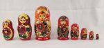 Boneca russa tipo matrioska em madeira, pintada à mão, composta por conjunto de 8 peças encaixáveis. Apresenta decoração policromada com figura feminina estilizada e motivos florais. Medidas: 20 x 9 cm (peça maior). 