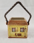 Inglaterra - Cesto decorativo de coleção em porcelana esmaltada, em formato de casa, com alça móvel e rica decoração em relevo policromado. Apresenta detalhes de fachada com janelas, porta e elementos ornamentais, com inscrição em relevo na base `Ye Olde Fireside` e marca `Made in England`.  Ausência de tampa Medidas: 13 x 12 cm sem alça. 