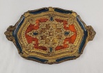 Bandeja veneziana decorativa em madeira, de formato recortado, com bordas trabalhadas e rica ornamentação em baixo relevo. Apresenta decoração policromada com motivos arabescos em tons dourados, azul e laranja.  Medidas: 43 x 28 cm. 