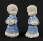 Par de castiçais em porcelana representando figuras infantis, com acabamento esmaltado em tons de branco e azul,, com suporte superior para vela. Medidas: 10 x 4 cm cada.