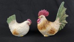 Duas esculturas decorativa em porcelana esmaltada representando galo e galinha com rica policromia e detalhamento naturalista nas penas. Marca Lefton China. Apresenta bicados nos pés do galo.. Medidas: 20 x 17 cm e  12 x 14 cm