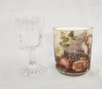 Duas peças, A) Taça em cristal transparente lapidado, apresentando rica decoração geométrica composta por estrelas, losangos e facetas. Haste curta e base igualmente trabalhada. Altura: 15 cm. B)  Vaso ou porta-vela em vidro decorado com composição floral policromada, destacando rosas, lilases, margaridas e borboletas. Medidas: 12 x 10 cm.