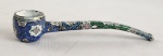 Cachimbo decorativo em metal esmaltado cloisonné, ricamente ornamentado com motivos florais e arabescos policromados. Apresenta fornilho cilíndrico e haste curva, integralmente revestidos por esmaltação decorativa. Comprimento: 14 cm.