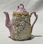 Pequeno bule de coleção em porcelana decoração floral em alto-relevo com detalhes dourados e esmaltação em tons de rosa e branco. Tampa e alça com elegante. Medindo: 14 x 13 cm. Bico com restauro e borda com um bicado.