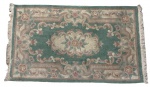 Tapete oriental em lã, de origem chinesa, apresentando rica decoração floral e arabescos em policromia suave sobre fundo verde-água. Cercadura ornamentada com flores estilizadas e acabamento com franjas nas extremidades. Medindo;148 x 89 cm.