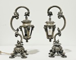 PRATA. Par de luminárias de mesa em prata portuguesa, teor 833 ml , com marca de contraste da águia, ricamente cinzeladas, hastes em elegantes volutas, lanternas sextavadas suspensas, cúpulas ornamentadas com motivos vegetalistas em relevo e bases tripés de exuberante decoração em estilo barroco/rocaille, apoiadas sobre pés recurvos. Peso total; 2,207 kg. Medidas: 33 cm de altura.Observação: uma das luminárias encontra-se em funcionamento; a outra necessita de revisão elétrica. Apresentam marcas compatíveis com o tempo e o uso.