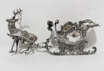 PRATA. Antiga carruagem decorativa em prata, representando elegante trenó no estilo vitoriano, ricamente executado com estrutura vazada e ornamentação em alto-relevo,  volutas, concheados, florões e molduras de gosto Rococó. Acompanha cervo cinzelado, atrelado por hastes decorativas. Necessita soldagem nas hastes de ligação entre o cervo e o trenó. Peso: 336 gramas.11 x 24 cm, pesando 335 g. Séc. XIX.