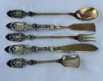 PRATA. Conjunto de cinco talheres para servir em prata, composto por colher vazada, espátula, garfo de servir, faca e pá para açúcar. Cabos ricamente ornamentados em relevo com volutas, concheados e motivos florais. Banho em vermill com desgastes. Medidas: de 15 a 20 cm.