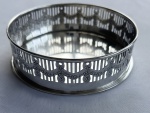 Antigo porta-garrafa em metal espessurado a prata, de formato circular, com corpo vazado, ornamentado por guirlandas em relevo e bordas lisas. Medidas: 3,5 x 11 cm.