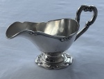 Fracalanza. Antiga molheira em metal espessurado a prata, com alça vazada e base elevada de contorno recortado. Corpo liso ornamentado por delicados frisos em relevo. Medidas: 8 x 19 x 8 cm.