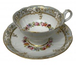 Antiga xícara para chá de coleção em porcelana branca esmaltada, ricamente ornamentada com reservas em douração e delicada guirlanda floral policromada ao centro. Bordas recortadas com filetes em ouro. Manufatura no verso