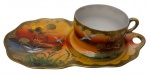 Antiga xícara de coleção em porcelana japonesa casca de ovo, acompanhada de Tea & Toast Tray (prato de apoio para chá e torradas), finamente decorada com paisagem oriental em policromia, representando aves em voo sobre lago ao entardecer, enriquecida por delicados motivos florais e arabescos em douração. Bordas recortadas e acabamento integralmente filetados a ouro. Manufatura no verso. Medidas: 21 x 12 x 6 cm.