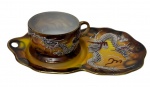 Antiga xícara de coleção em porcelana japonesa casca de ovo, estilo Dragonware (Moriage), acompanhada de Tea & Toast Tray (prato de apoio para chá e torradas), ricamente ornamentada com dragão oriental em relevo, realçado por esmaltação branca e policromia sobre fundo marmorizado em tons de âmbar, castanho e negro. Bordas recortadas e acabamento integralmente filetados a ouro. Manufatura no verso. Medidas: 21 x 12,5 x 6,5 cm.pequeno bicado na xícara.