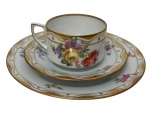 Mäbendorf 1882. Antigo trio para chá de coleção em porcelana alemã esmaltada, finamente decorado com delicadas reservas florais policromadas, largas faixas onduladas e filetes em ouro. Composto por xícara, pires e prato para sobremesa, todos com bordas recortadas e acabamento em douração. Prato medindo 19 cm.  Marca da manufatura no verso. Apresenta fio de cabelo na xícara.