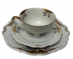 C.T. Tielsch-Altwasser, Germany. Antigo trio para chá de coleção em porcelana branca esmaltada, finamente decorado com delicadas reservas florais policromadas, ornamentos em relevo e detalhes em douração. Composto por xícara, pires e prato para sobremes, bordas recortadas. Prato medindo 19 cm. Marca da manufatura no verso.
