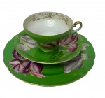 Antigo trio para chá de coleção em porcelana esmaltada, finamente decorado com exuberantes reservas florais policromadas sobre fundo verde, ornamentos em relevo e acabamento em douração. Composto por xícara, pires e prato para pão, bordas recortadas e filetadas a ouro. Prato medindo;18 cm. Manufatura no verso. Apresenta pequeno bicado na borda da xícara.