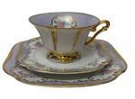 Mauá. Antigo trio para chá de coleção em porcelana branca esmaltada, finamente decorado com delicadas reservas florais policromadas sobre fundo em suave tom lilás, enriquecidas por elegantes arabescos e larga douração. Composto por xícara, pires e prato para pão, de formato recortado e  filetados a ouro. Prato para pão medindo 17,6 cm. Manufatura no verso.