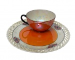 P.A.L.T. Czecho-Slovakia. Antiga xícara de coleção em porcelana iridescente, acompanhada de pires rendado (pierced), decorada em vibrante tonalidade alaranjada com acabamento nacarado e delicados detalhes em relevo. Alça na cor preta. Conjunto Art Déco, marcado na base. Medida do pires: 19 cm.