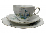Antigo trio para chá em porcelana, composto por xícara de coleção, pires e pratinho de pão, delicadamente moldados com bordas onduladas, decorados com motivos florais policromados em tons de azul, verde e lilás, realçados por elegante douração nas bordas e na alça. Med: 17 cm. O prato apresenta pequeno bicado na base.