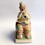 Melody in Motion - Escultura musical colecionável produzida em biscuit representando palhaço tocando instrumento com rica policromia. Manufatura WACO made in Japan. Década de 1970. Não testado. Med 29,5 x 13 x 16 cm.