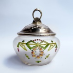 Compoteira Art Nouveau em vidro translúcido decorada com laços e guirlandas, tampa em metal prateado com pega vazada. Falhas na prateação. Med 15 cm altura e 10 cm de diâmetro. 