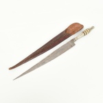 CUTELARIA NORDESTINA, um (1) antigo punhal com lâmina em aço, sem gume,  empunhadura confeccionada com discos sobrepostos e unidos de materiais variados, bainha em couro, medindo 29 cm comprimento, sinais de uso, vide foto.