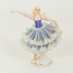 ESCULTURA, uma (1) figurativa feminina representando bailarina, confeccionada em porcelana, policromada, vestido de renda na técnica de barbotina (tecido de algodão tipo gaze embebido em massa líquida de porcelana que serve para moldar a renda na peça antes de ir ao forno), com pequenas perdas na renda, braço quebrado e colado, arremates a ouro, medindo 10 cm altura, vide foto.