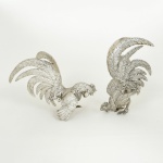 ESCULTURAS, duas (2) representando galos de briga, medindo a maior 29 cm comprimento, confeccionadas em metal prateado, sinais de uso, vide foto.