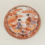 PORCELANA JAPONESA, uma (1) caixa com tampa, pintada a mão em policromia, predominância da cor vermelha, representando paisagem com gueixas, arremates a ouro, marca SUZUKI COMPANY em caracteres, Made in Japan, medindo 11 cm diâmetro, vide foto.